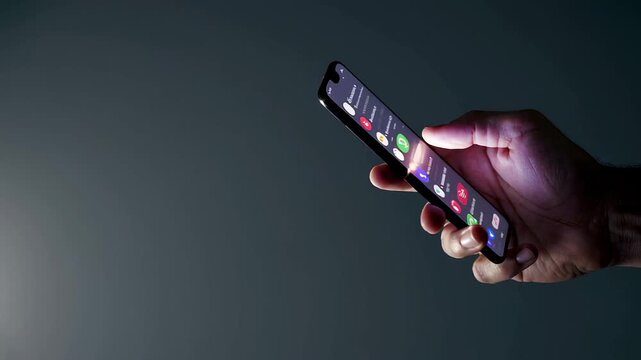 Hand holding modern smartphone while scrolling through social media applications, revealing digital connectivity against minimalist dark gray background