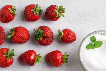 Top view of ripe organic strawberries arranged in rows next to a bowl of white sugar with mint leaf on gray concrete table © Taborisova