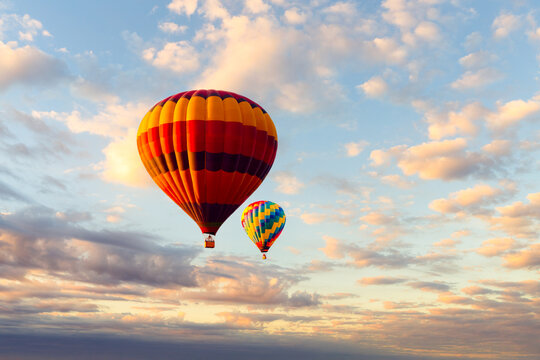 Two colorful hot air balloons flying high in the beautiful sky filled with clouds during sunrise.