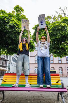 Two people standing on a rainbow bench holding equality signs