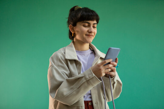 Smiling young woman using mobile phone against green background