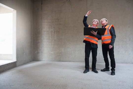 Two men wearing safety vests talking in building under construction