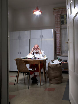 Stressed Santa Claus reading Christmas mail in kitchen at night