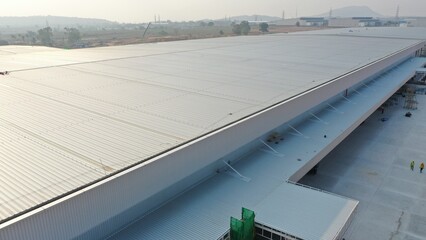 Vast Industrial Warehouse: An expansive, modern warehouse with a long, gleaming metallic roof dominates the landscape, signifying large-scale logistics and industry. © Rassarin