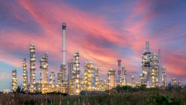 Industrial Powerhouse at Dusk: A sprawling oil refinery complex illuminated against a dramatic sky painted with hues of pink and orange, symbolizing energy production and industrial might.