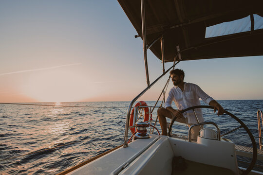 Skipper navigating a sailboat on the sea at sunset
