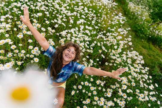 Smiling adult with arm outstretched in summer garden with daisy