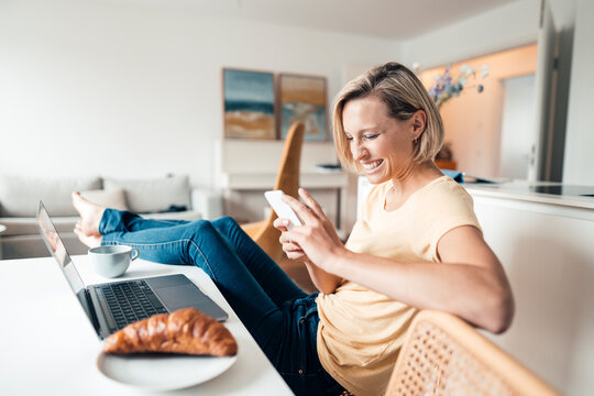 Smiling businesswoman with feet up using mobile phone while working at home