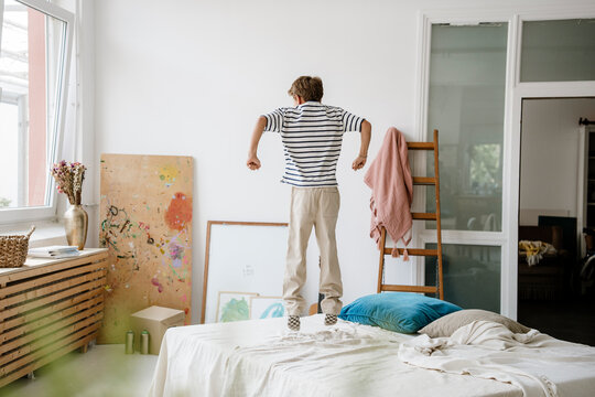 Boy jumping playfully on a bed in an apartment bedroom