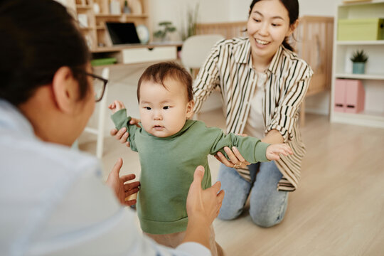 Father and mother supporting daughter taking first steps at home
