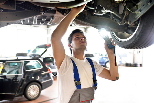 Mechanic examining underbody of a car in a garage