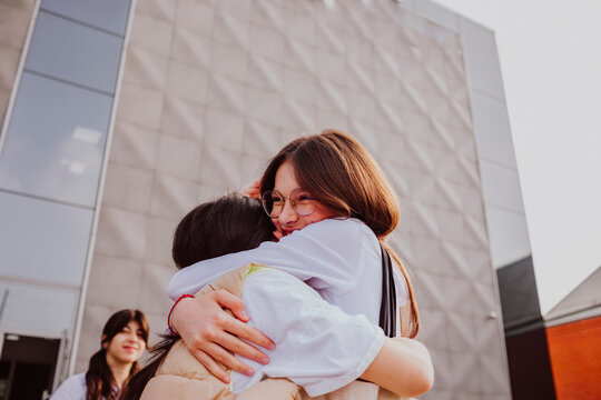 Happy girl embracing friend standing in front of school building