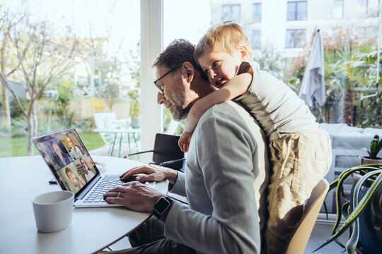 Little boy hugging father from behind, while working from home