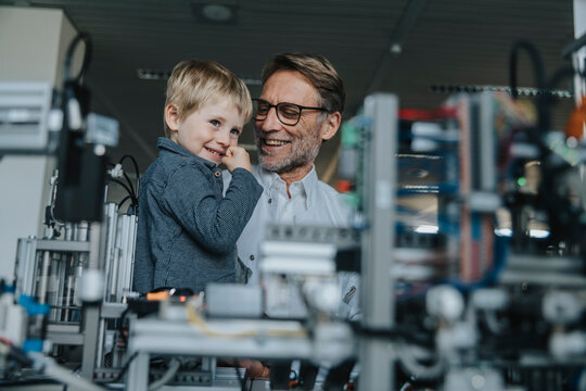 Smiling male scientist showing machinery to son in laboratory at factory