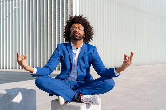 Businessman with eyes closed practicing lotus yoga pose sitting on concrete block