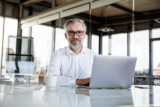 Portrait of confident businessman with laptop at desk in office