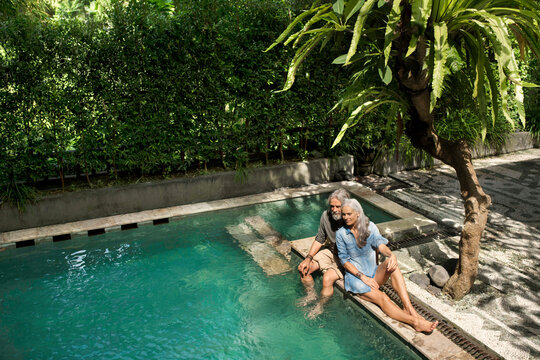 Senior man taking selfie at poolside while his wife is playing the guitar