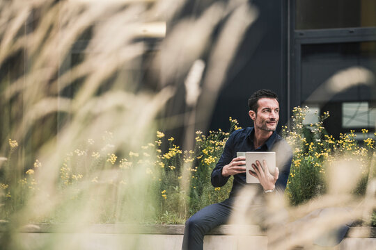 Businessman sitting outside, taking a break, drinking coffee, using digital tablet