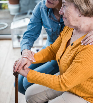 Caregiver comforting a patient holding a walking stick indoors
