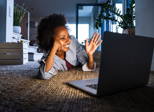Woman smiling and waving during video call on laptop at home