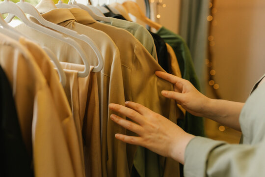 Hands of woman choosing dress from clothes rack in store