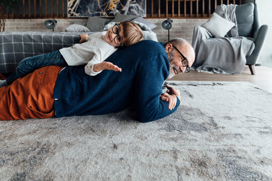 Smiling cute boy lying on grandfather's back at home
