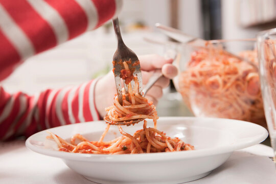 Hands twirling spaghetti with fork and spoon at the dining table