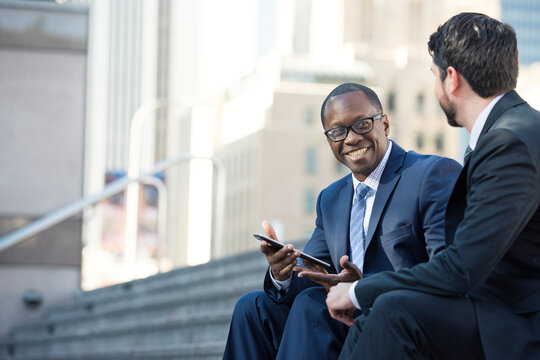 Smiling businessmen sitting on stairs sharing tablet with colleague