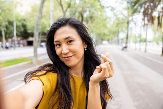 Smiling woman making taking selfie on tree-lined street in the city