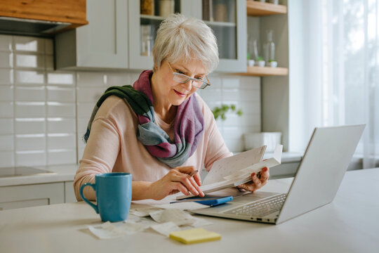 Woman calculating tax and budget with laptop in kitchen
