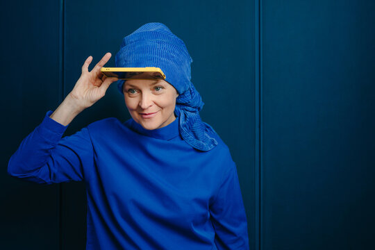 Woman holding yellow smartphone like a visor against a blue wall