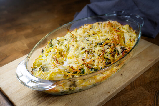 Casserole with cauliflower, spinach, and spaghetti, baked with egg and cheese in a glass dish, on a dark rustic wooden table, homemade vegetarian meal, selected soft focus