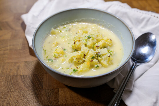 Cauliflower soup with herbs and spices in a bowl, napkin and spoon on a rustic wooden table, homemade healthy vegetarian meal, selected focus
