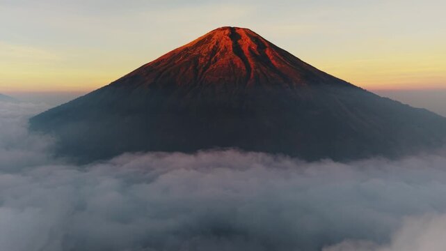Aerial view of Mount Sindoro rising above a thick sea of clouds during golden hour in Kecamatan Kedu, Jawa Tengah, Indonesia.