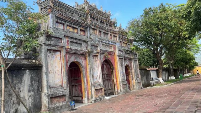 Weathered three arch imperial gate beside tree lined walkway at Hue Imperial City. Historic Vietnamese architecture showcasing cultural heritage, craftsmanship and timeless imperial history.