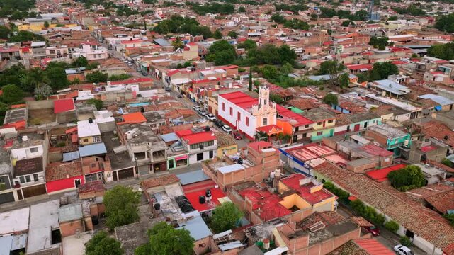 Aerial view of Capilla Cruz Blanca church in Tuxpan Jalisco, with surrounding homes in city center residential area. Drone ascending reveal of Cihuapilli Hill