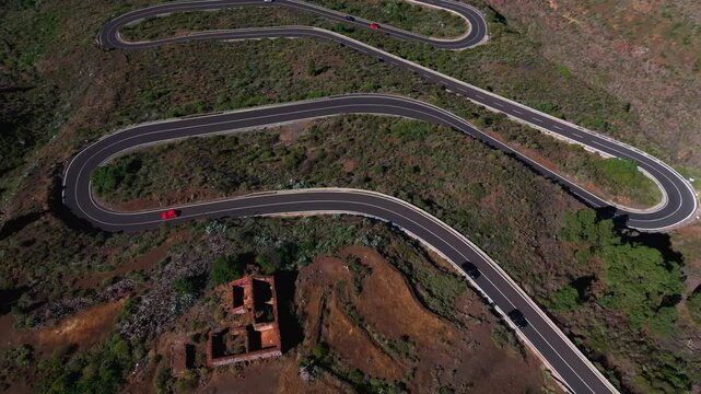 Aerial view of winding mountain road with cars crossing volcanic terrain and ruins