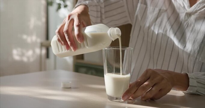 Close up of Asian Woman Hand Pouring Soy Milk into Glass on Table in Cozy Living Room