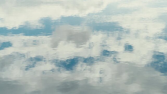 Soft cloud shapes and blue sky appear as an abstract reflection across gently rippling water, creating a clean natural background with subtle texture, calm movement, and generous copy space.
