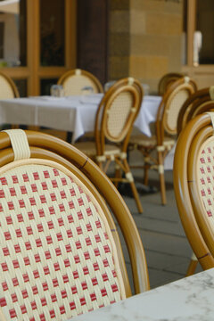 Cozy outdoor restaurant terrace with classic woven caf&eacute; chairs and tables, creating a warm and inviting atmosphere. Elegant European caf&eacute; setting with shallow depth of field, ideal for hospitality, tr