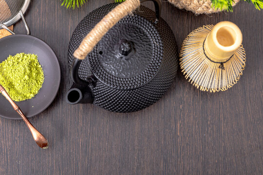 Matcha tea powder with bamboo whisk and black iron teapot on dark wooden table. Japanese tea ceremony preparation with organic green tea leaves. Healthy natural lifestyle tradition