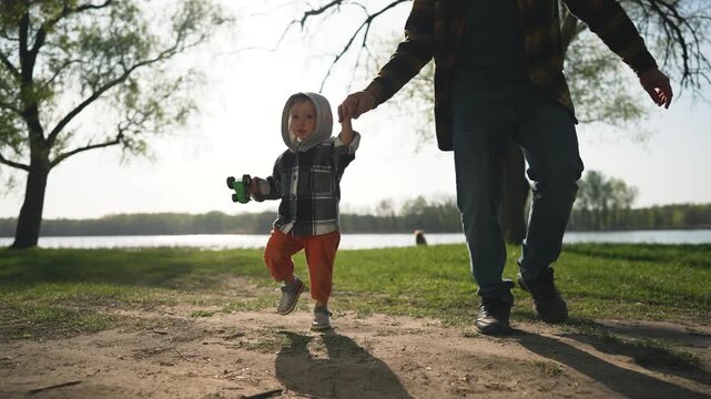 Family playing outdoors in park. Happy child holding father hand, enjoying playful time. Family bonding in nature. Joyful outdoor play in park. Smiling child. Family fun, outdoor park activity