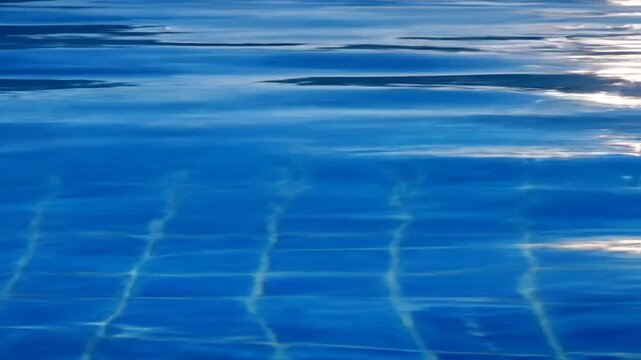 Blue swimming pool water rippling under bright sunlight with caustic reflections.