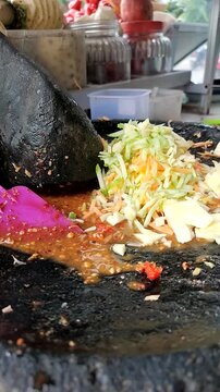 Hands slicing fresh water apples over a traditional stone mortar filled with spicy chili peanut sauce to make Indonesian shaved rujak.