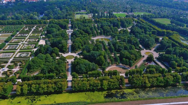 Aerial drone view of Herrenhausen Gardens with tree-lined avenues, fountain pools, and formal baroque parterres in Hannover, Germany, summer daytime.