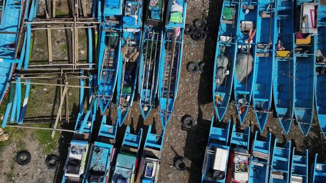Aerial view of blue fishing boats moored on the sandy shore at Pantai Pedalen in Kecamatan Ayah, Jawa Tengah, Indonesia.
