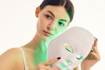 Beauty portrait of woman with green LED face mask and glowing skin. Concept of selfcare products,...