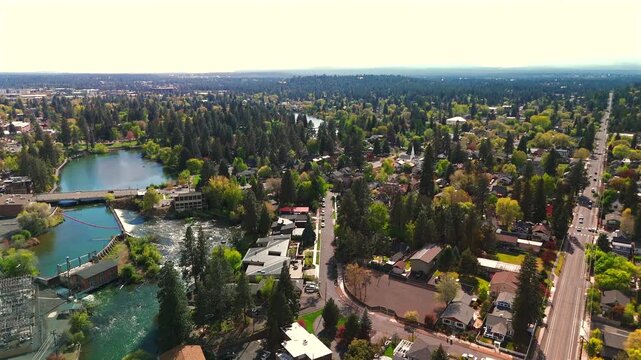 Drone reveals a small dam on a river creating a calm reservoir surrounded by trees and natural scenery