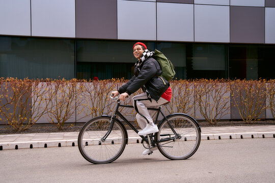 Handsome young African American man riding a bicycle in stylish attire through the city streets
