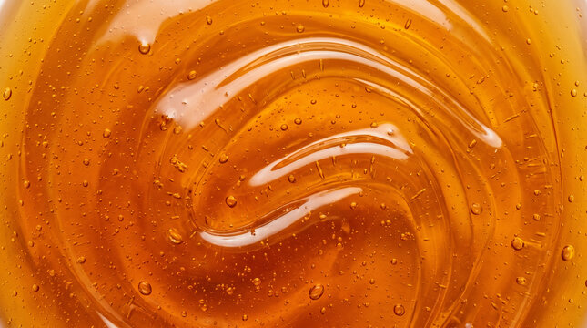 Close-up of thick organic golden honey texture with swirling waves and tiny air bubbles, sweet translucent amber maple syrup or cosmetic gel background
